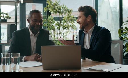 Uomini eterogenei colleghi team aziendali che condividono idee lavoro portatile discussione durante una riunione d'ufficio sorridente due uomini d'affari multirazziali entusiasti Foto Stock