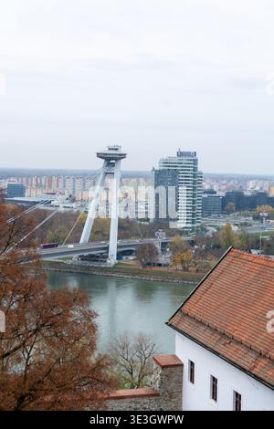 La vista di un moderno ponte in pilone bianco si estende graziosamente lungo il fiume scintillante, sullo sfondo di un moderno skyline della città, Bratislava, Bratislava R. Foto Stock