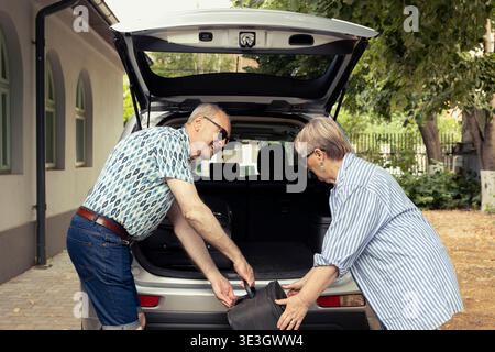 Gli anziani caricano l'auto con le valigie e si sentono allegri per il nuovo viaggio in auto, emozionati mentre si preparano per una vacanza rilassante. La coppia in pensione ama viaggiare e vivere insieme in modo felice. Foto Stock