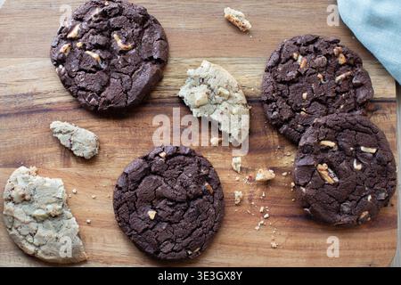 biscotti appena sfornati sparsi su un tagliere di legno. La collezione comprende biscotti fondenti con due gocce di cioccolato Foto Stock