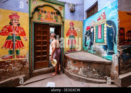 Un uomo cammina attraverso una porta a Varanasi fiancheggiata da pittoreschi murali di figure tradizionali e da un elefante sulle pareti blu. Foto Stock