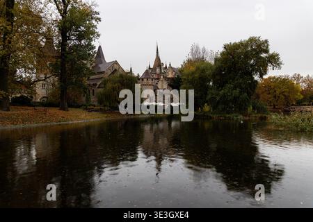 Vista del maestoso castello di Vajdahunyad, che si specchia nel lago naturale sotto un cielo grigio, circondato da alberi autunnali con foglie cadute, Budapest, Ungheria Foto Stock