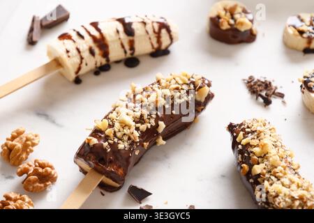 Lecca di banana surgelata o lecci con noci spruzzare per i bambini su bianco. Dolci vegani fatti in casa. Primo piano. Foto Stock