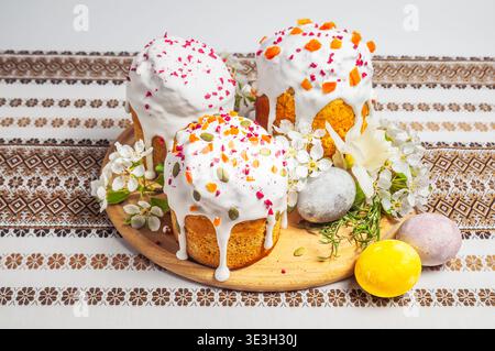 Tre torte pasquali splendidamente decorate, note come kulich o paska, sono disposte con uova dipinte e delicati fiori primaverili su una tavola di legno Foto Stock