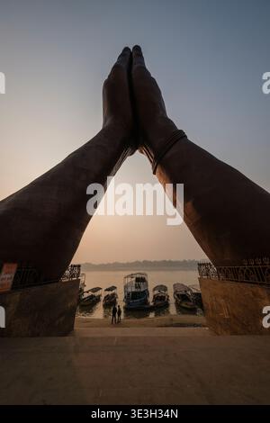 Una vista dall'angolo basso mostra le mani di Namo Mudra a Namo Ghat a Varanasi, incorniciando diverse barche attraccate sul fiume Gange all'alba. Foto Stock