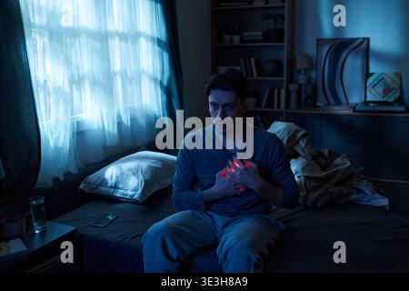 Uomo adulto seduto sul letto che prova dolore al torace di notte Foto Stock
