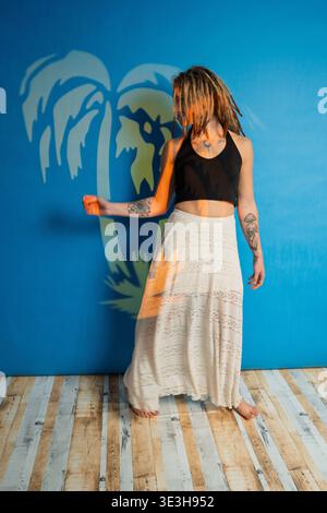 Donna con dreadlock e tatuaggi in posa su sfondo blu con proiezione di palma Foto Stock