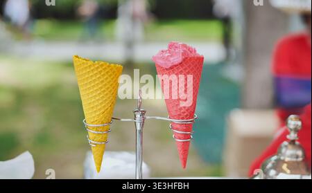 Gelato al sorbetto di fragole in un cono di waffle rosa con un cono giallo vuoto Foto Stock