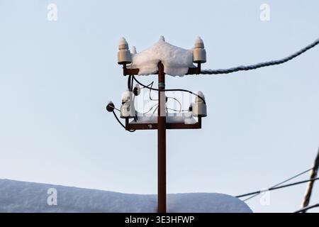 Ambientazione invernale caratterizzata da un isolatore elettrico coperto da neve incontaminata, contro un cielo limpido. Il palo e i cavi intemprati aggiungono un tocco di fascino rustico Foto Stock