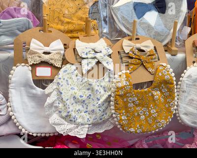 Bavaglini floreali e fiocchi coordinati disposti presso uno stand del mercato degli accessori fatti a mano. Accessori essenziali per l'allattamento dei neonati, stile della nursery, selezione di regali e bo Foto Stock