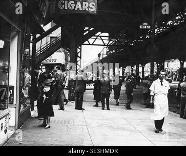 Questa accattivante fotografia di strada di Angelo Rizzuto, probabilmente degli anni '1940, cattura la vita quotidiana e la moda dei newyorkesi in Third Avenue e 14th Street. La scena è dominata dai binari del treno sopraelevati, sotto i quali i pedoni vestiti d'epoca navigano nel vivace paesaggio urbano. Foto Stock