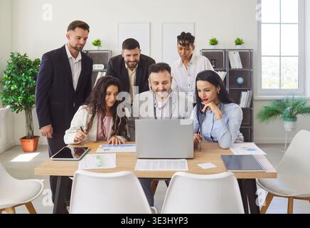 Gruppi diversificati, professionisti dell'ufficio che si riuniscono intorno alla scrivania per guardare un notebook, documentare e discutere Foto Stock