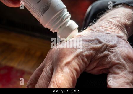 Uomo anziano che applica Biofreeze roll-on per alleviare il dolore all'artrite nella mano, 2026, Stati Uniti Foto Stock