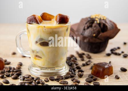 Vista laterale della bevanda a base di caffè ghiacciato con latte, cubetti di ghiaccio sparsi sul tavolo, decorati con chicchi di caffè. Ripresa in studio. Concetto di cubetti di ghiaccio per caffè f Foto Stock