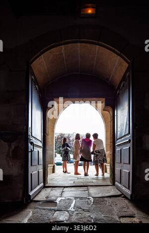 Quattro donne sono sagomate contro l'esterno luminoso mentre si trovano sulla porta ad arco in pietra della chiesa di Saint-Guigner a Pluvigner, Morbihan, Brit Foto Stock