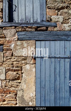 Pareti in pietra testurizzata e persiane in legno blu con una porta che incarna l'architettura tipica di Baden, Morbihan, Bretagna, Francia. Foto Stock