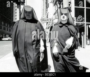 Questa accattivante fotografia di strada, probabilmente catturata da Angelo Rizzuto negli anni '1950 o '1960, raffigura due suore in abitudini tradizionali che camminano lungo un vivace marciapiede di New York. Gli stili contrastanti del loro abbigliamento sullo sfondo urbano offrono uno sguardo alla vita quotidiana e alla moda dell'epoca. Foto Stock