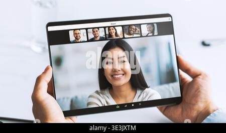 Un giovane uomo d'affari utilizza un tablet per videochiamate su un tavolo bianco con blocchi appunti e display digitale Foto Stock