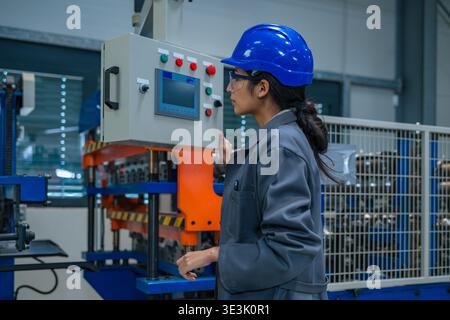 Un ingegnere indiano lavora con macchinari in una fabbrica, indossando attrezzature di sicurezza e concentrandosi sul suo lavoro in un'area di produzione. Foto Stock