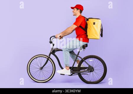 Young Man Rides Bicycle con zaino davanti allo sfondo viola durante il giorno Foto Stock