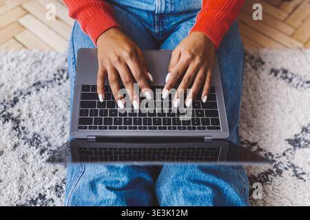 Donna che usa il laptop su un tappeto mentre indossa un pullover rosso e un Blue Jeans a casa Foto Stock