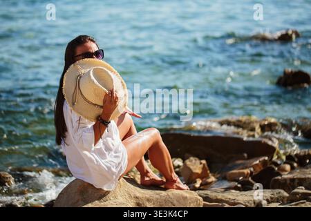 Donna che gode della vista sul mare con il cappello in mano Foto Stock