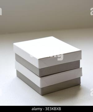 Immagine ad alta risoluzione di caselle quadrate bianche con basi grigie impilate ordinatamente su un tavolo bianco. Composizione minimalista che rappresenta l'imballaggio, il branding, Foto Stock