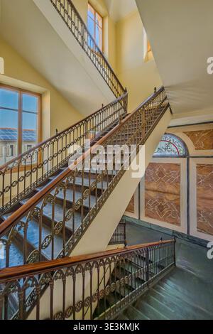 Scalinata interna in un edificio storico caratterizzato da scale in pietra e ringhiere in ferro battuto, nell'eclettico stile architettonico italiano dell'orecchio Foto Stock