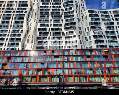 Vista ad angolo basso di un suggestivo edificio residenziale alto e contemporaneo caratterizzato da una facciata bianca ondulata con finestre di forma irregolare e. Foto Stock