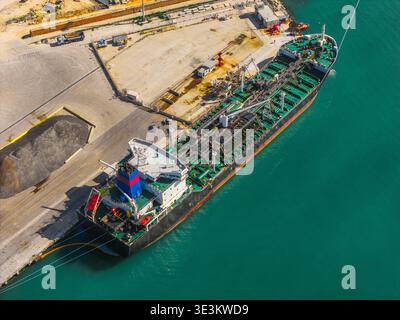 La vista aerea di un'enorme nave cisterna, un titano di acciaio e colore, contrasta con le tranquille acque turchesi del porto, ancorate al molo industriale, o. Foto Stock