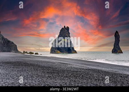 La spiaggia di sabbia nera di Reynisfjall, in Islanda, mostra le montagne marine che si innalzano dall'oceano sotto un cielo grigio. Le onde si infrangono sulla riva. Foto Stock