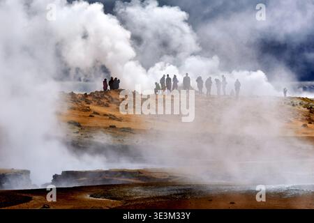 La gente cammina vicino alle sorgenti termali di hverir e ai geyser in Islanda. Il vapore sale da terra, creando un paesaggio unico e attivo. Foto Stock