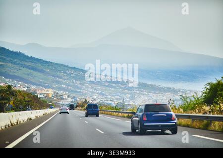 Vista sull'autostrada con auto che attraversano Tenerife, le Isole Canarie, la Spagna, con la sagoma nebbiosa del monte Teide sullo sfondo. Strada panoramica Foto Stock
