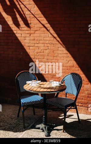 Piccolo tavolo e sedie adagiati sotto la luce del sole contro un muro di mattoni rossi in un'area caffè Foto Stock