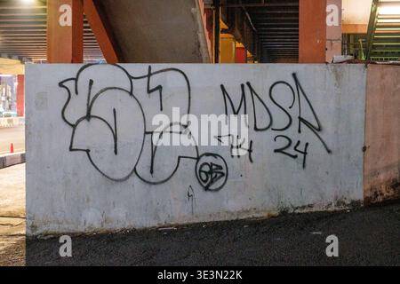 I segni di graffiti coprono una parete di cemento sotto un cavalcavia. L'inchiostro nero indica "MDSA" e "714 24" sulla superficie. Il muro ha una consistenza ruvida e macchiata. U Foto Stock