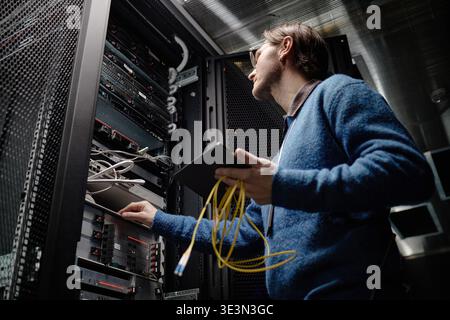 Adulto uomo caucasico che gestisce le apparecchiature server nella sala dei data center Foto Stock