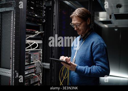 Uomo adulto caucasico che gestisce le apparecchiature server utilizzando un tablet digitale Foto Stock