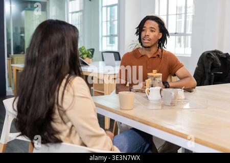 Diversi colleghi discutono di progetti a tavola nell'area di coworking con caraffa d'acqua e laptop Foto Stock
