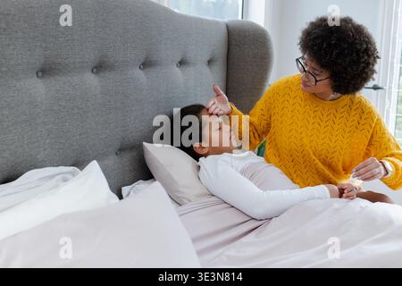 Madre e figlia afroamericana che controllano la temperatura in camera da letto usando un termometro, copia spazio Foto Stock