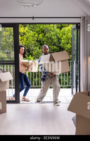 Diverse coppie che trasportano scatole mobili e piante in vaso attraverso porte di vetro nel soggiorno Foto Stock