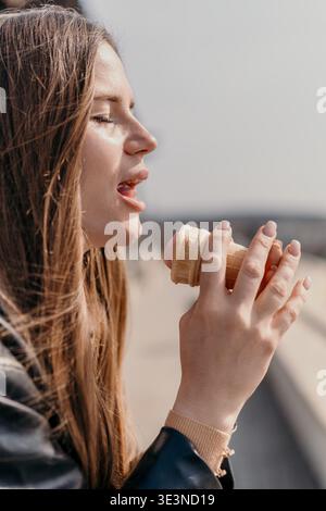 Donna che mangia gelato all'aperto mentre tiene in mano un delizioso cono di waffle alla fragola in una giornata di sole Foto Stock