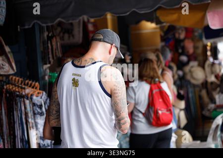 BANGKOK, THAILANDIA-Mar 8,2026: Turista maschile che esplora il mercato di strada e utilizza smartphone, profilo laterale, a Tha Chang. Foto Stock