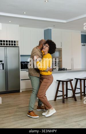 Coppie afroamericane che ballano e si abbracciano in una cucina moderna con frigorifero in acciaio inossidabile Foto Stock