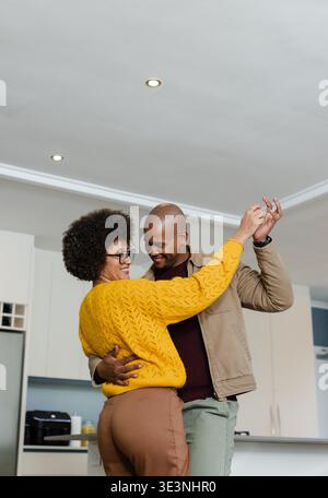 Diverse coppie che ballano e tengono le mani in alto nella cucina casalinga con macchina per il caffè su un ripiano bianco Foto Stock