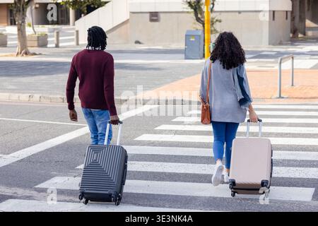 Diverse coppie che camminano attraverso la passerella a righe all'angolo della strada tirando le valigie Foto Stock