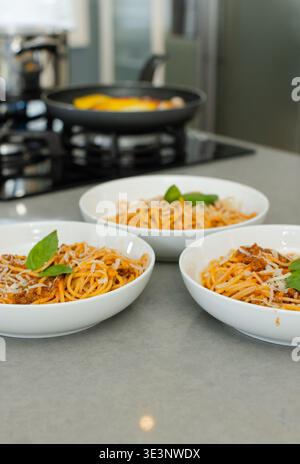 Tre ciotole in ceramica con spaghetti alla bolognese, formaggio fuso e basilico su un piano di appoggio grigio Foto Stock