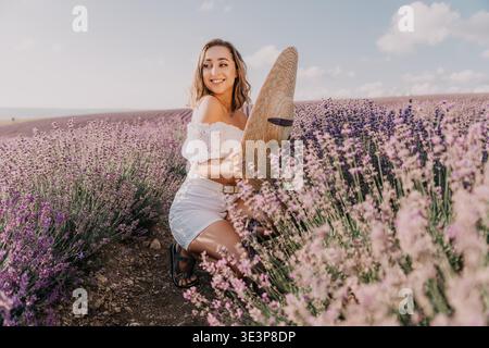 Donna lavanda estate giovane donna sorridente e con un cappello di paglia mentre accovacciata in un bellissimo campo di fiori viola Foto Stock