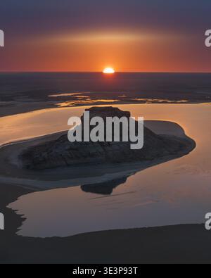 Vista aerea di una formazione rocciosa solitaria che si innalza da acque poco profonde sotto un vibrante tramonto, Aktau, regione di Mangystau, Kazakistan. Foto Stock