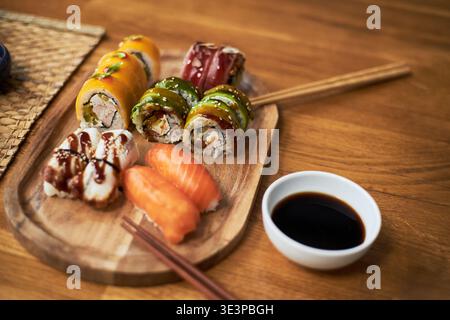 Cucina asiatica tradizionale con sushi roll e nigiri assortiti disposti su un piatto di legno con bacchette e salsa di soia, evidenziando la presentazione e la varietà culinaria culturale Foto Stock