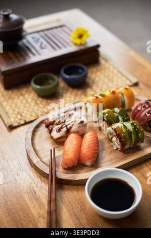 Sushi roll e nigiri assortiti disposti su tavola di legno con salsa di soia e bacchette sul tavolo, cucina tradizionale asiatica che rappresenta un'esperienza culinaria culturale Foto Stock